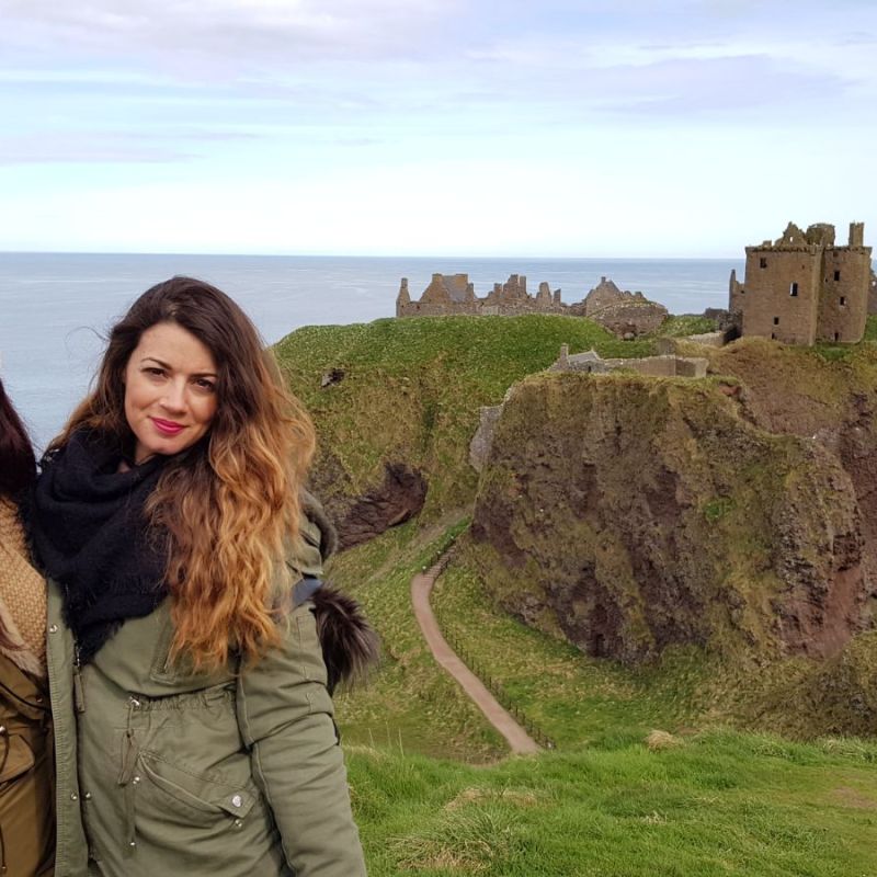 a person standing in front of a body of water with Dunnottar Castle in the background